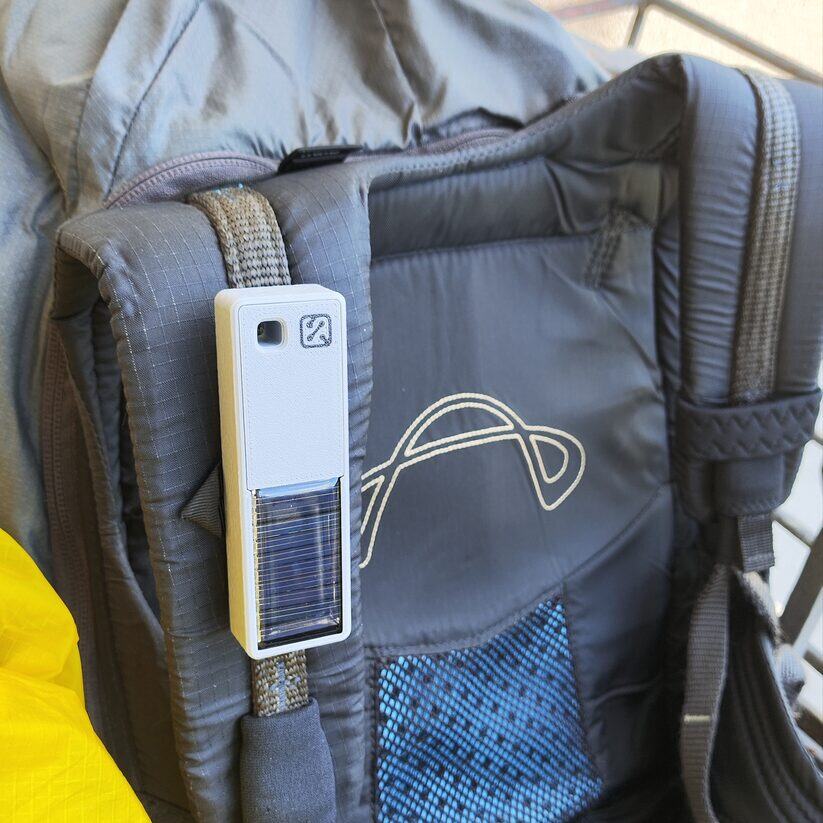 Mounted on a harness shoulder strap — solar panel facing out, antenna block up